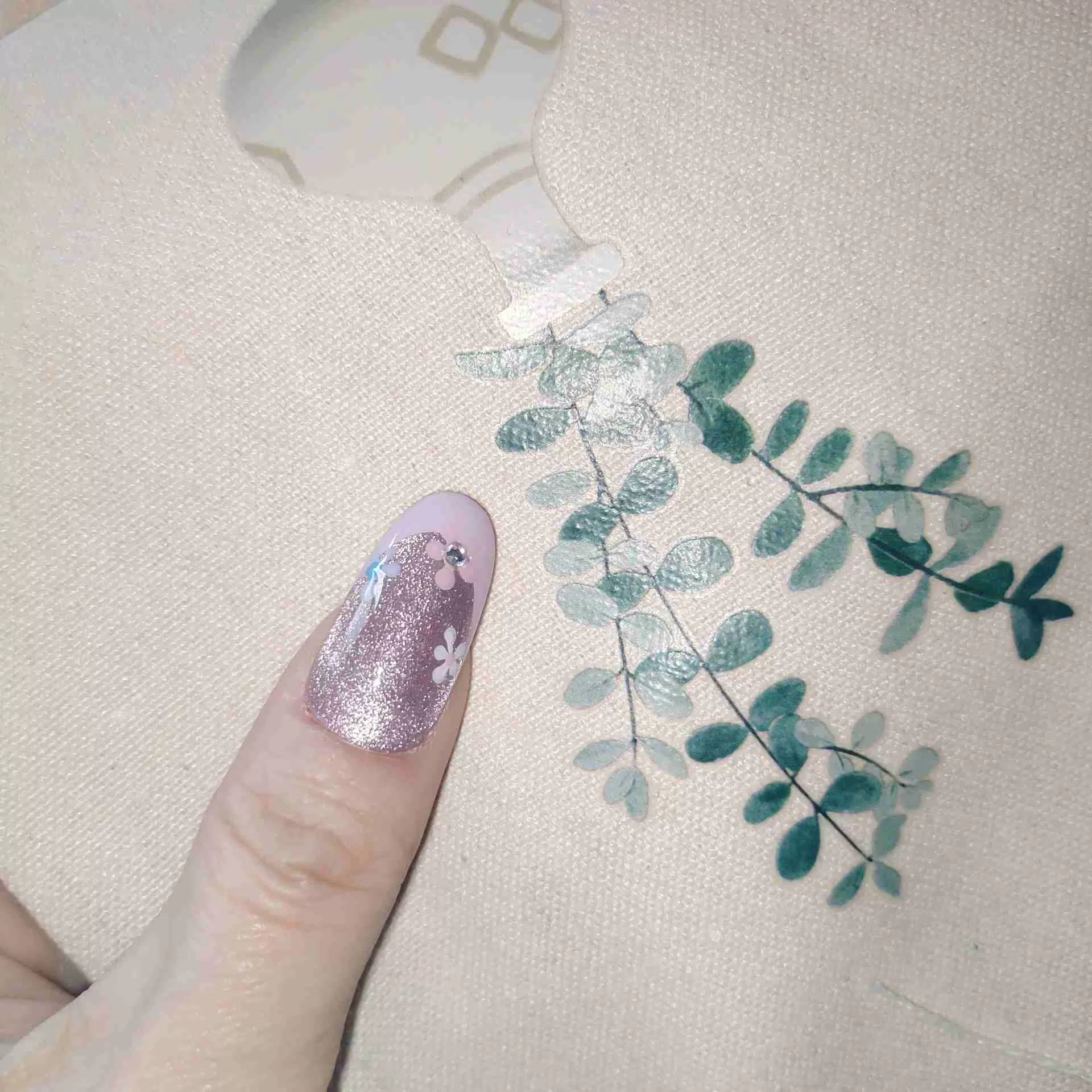 A close-up of a hand showcasing long, oval press-on nails with a sheer, sparkling mauve-pink cat-eye base and elegant pastel pink French tips, delicately decorated with tiny hand-painted blue and white flowers and miniature rhinestones. — photo 4