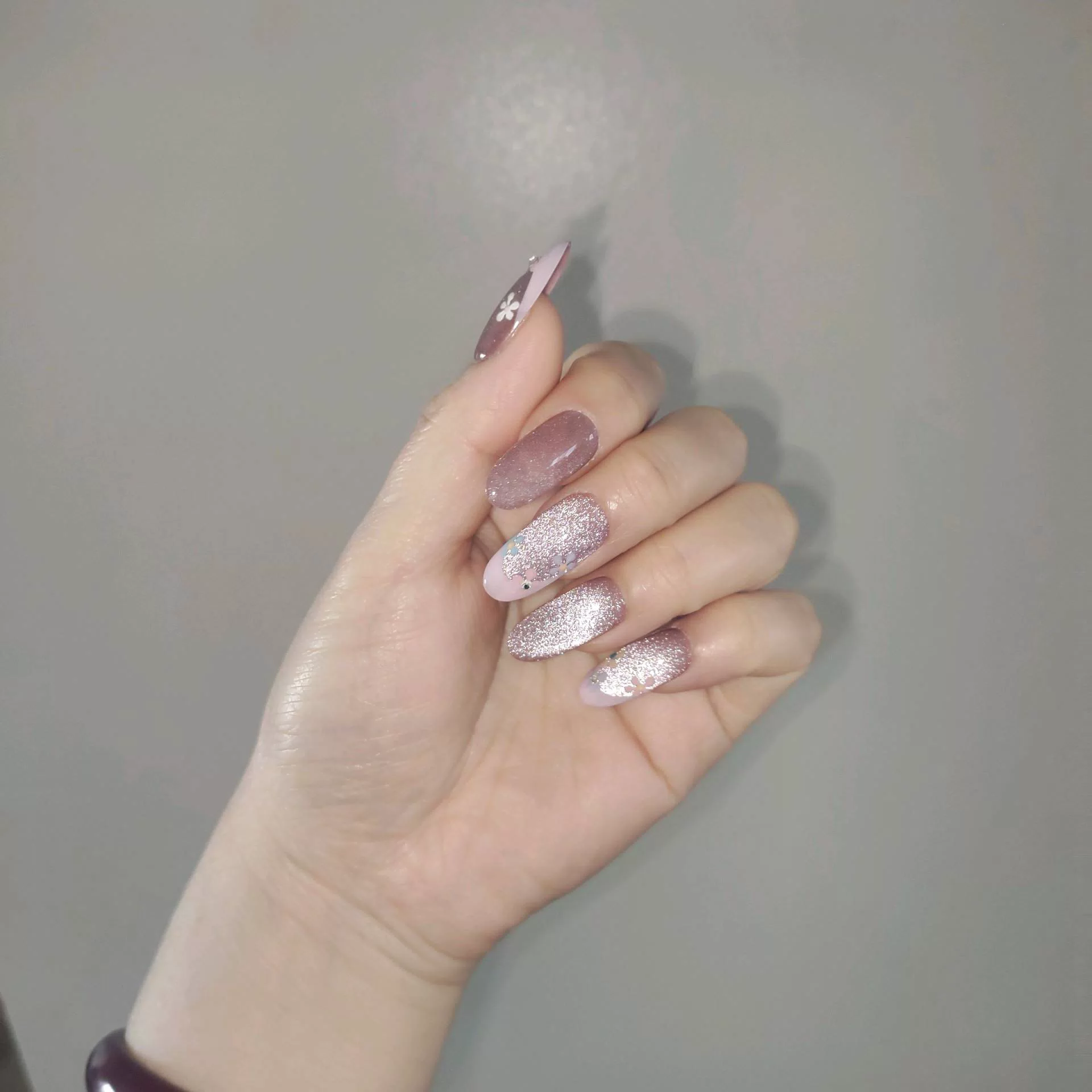 A close-up of a hand showcasing long, oval press-on nails with a sheer, sparkling mauve-pink cat-eye base and elegant pastel pink French tips, delicately decorated with tiny hand-painted blue and white flowers and miniature rhinestones. — photo 2