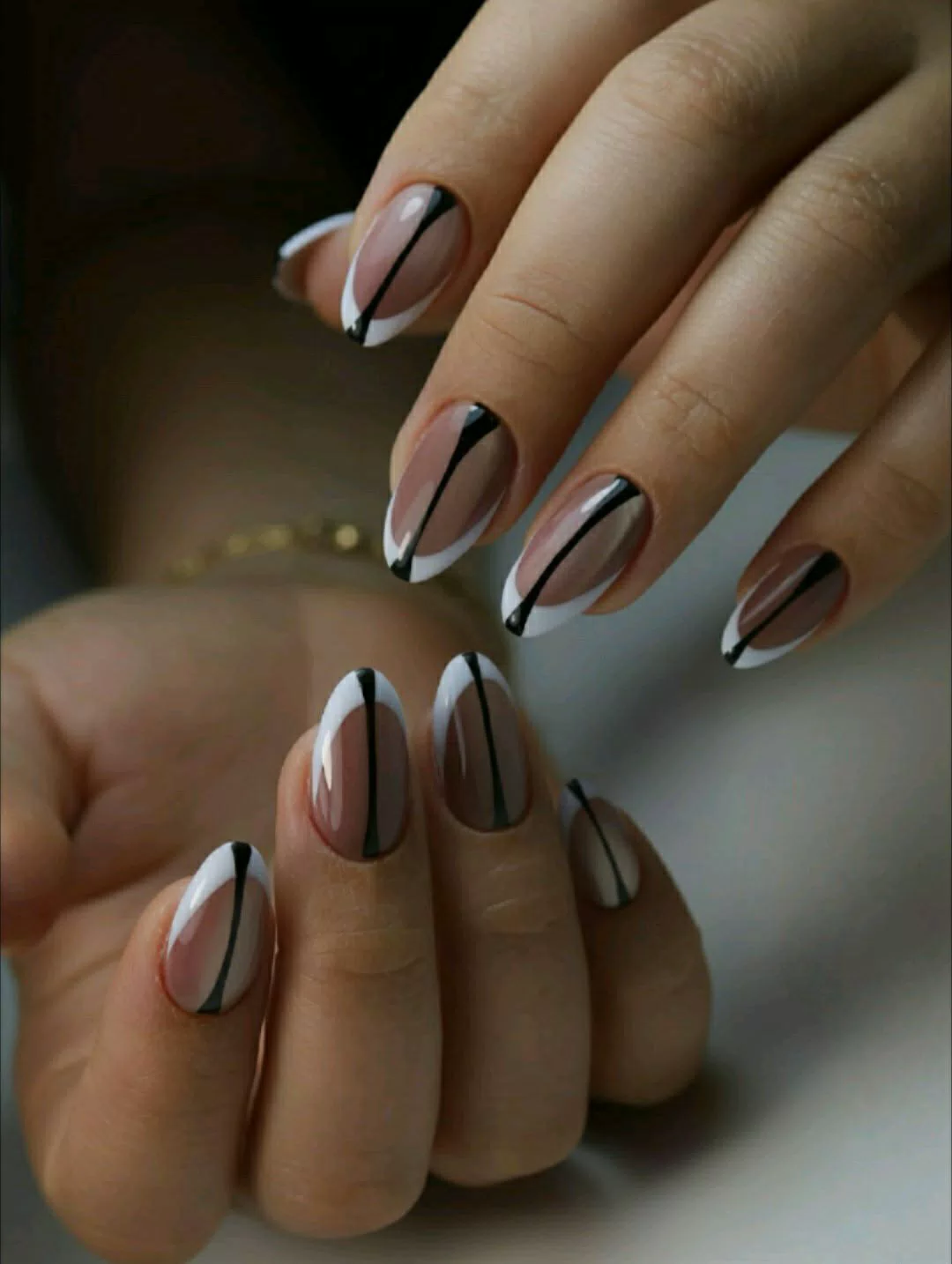 A close-up of hands displaying medium almond-shaped press-on nails with a sheer nude base, a classic crisp white French tip, and a single thin black vertical line running down the center of each nail.