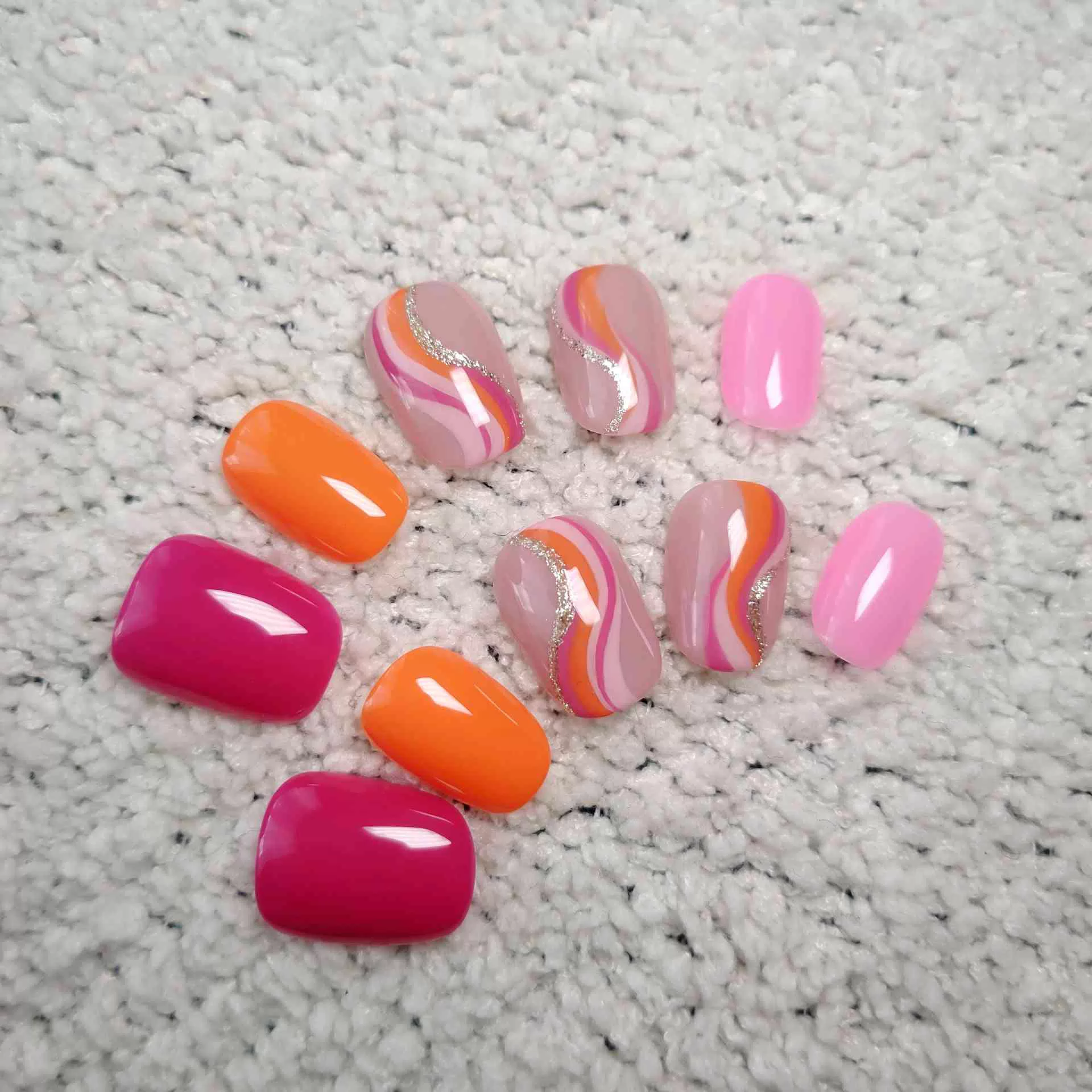 A hand showcasing short, rounded oval press-on nails with a mix of solid vibrant orange, hot pink, and abstract wavy swirl patterns in pink, orange, and white over a natural nude base. — photo 4