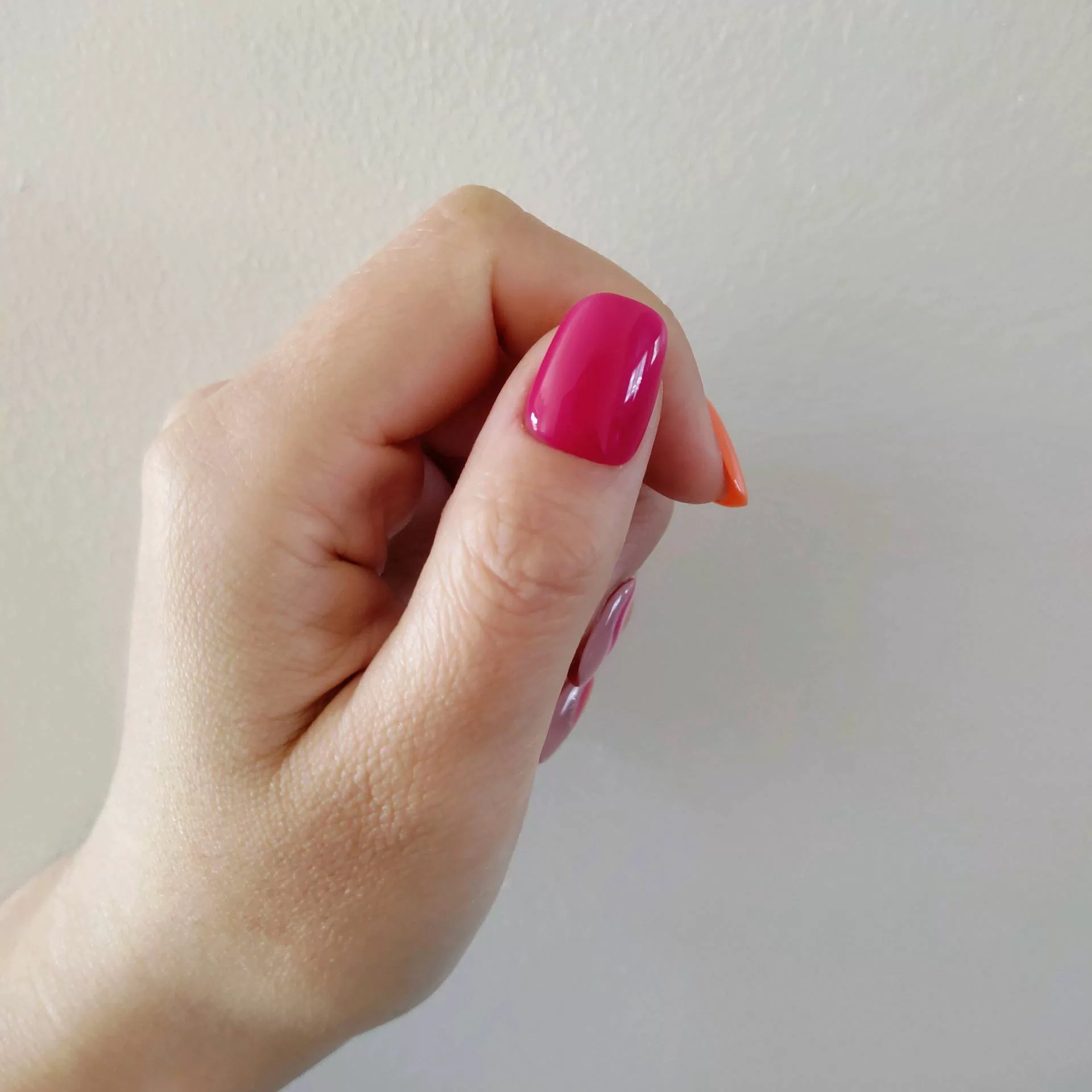 A hand showcasing short, rounded oval press-on nails with a mix of solid vibrant orange, hot pink, and abstract wavy swirl patterns in pink, orange, and white over a natural nude base. — photo 2