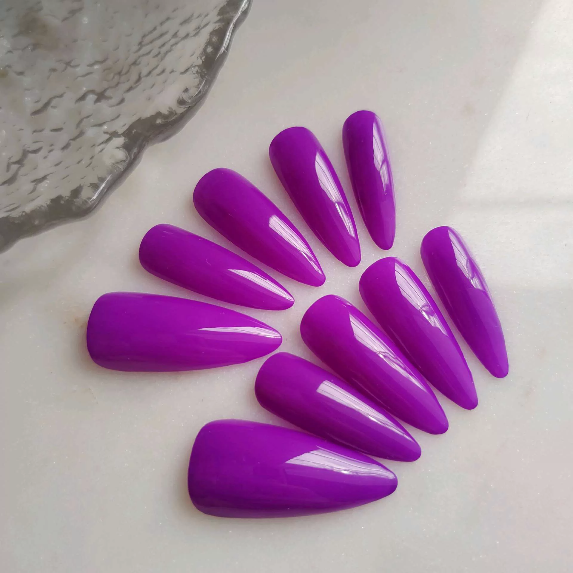 A flat-lay display of long, tapered almond-stiletto press-on nails in a solid, vibrant, ultra-glossy magenta purple color. — photo 2