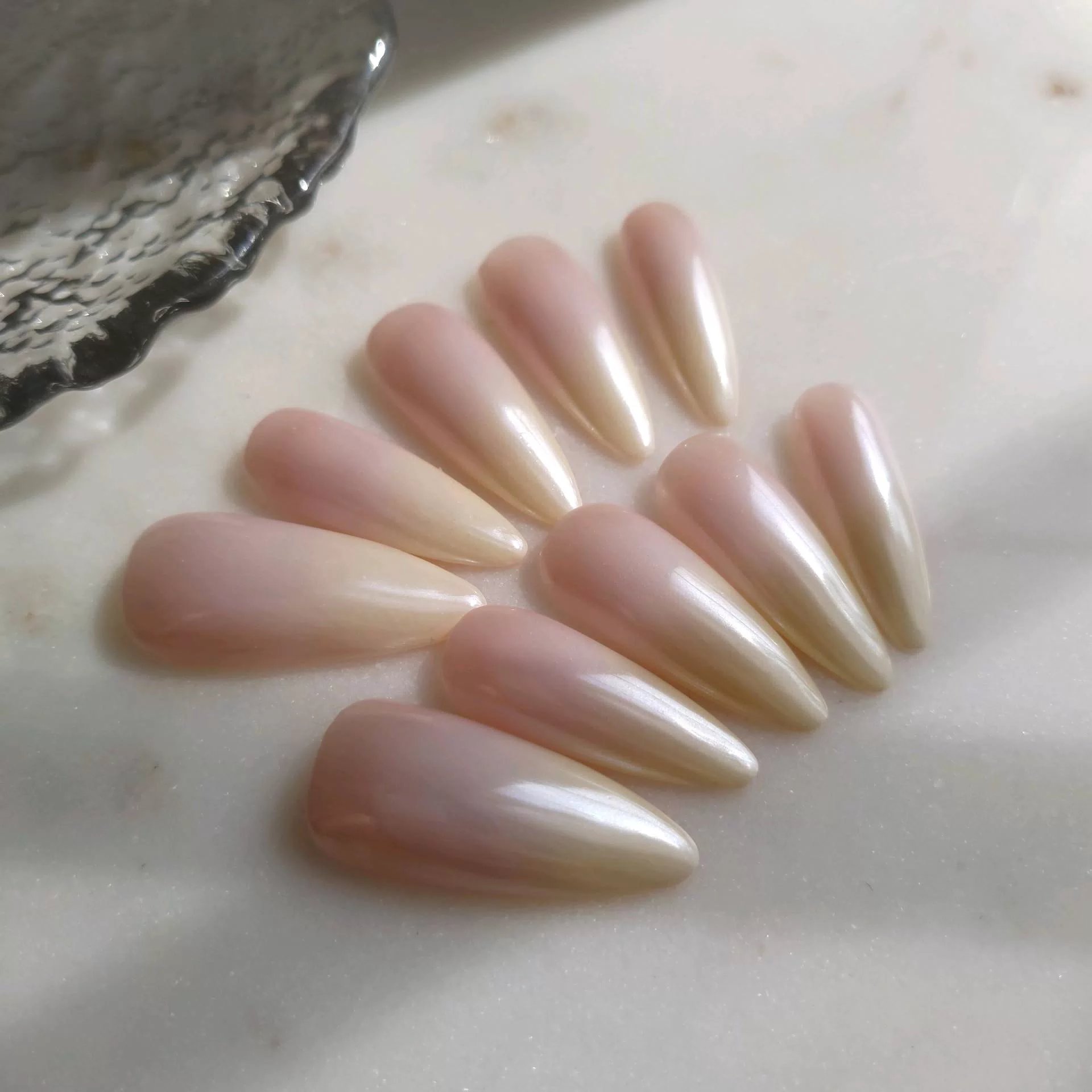 A flat-lay display of long, tapered almond press-on nails featuring a soft vanilla-nude ombre base coated in a high-shine, iridescent pearl chrome glaze. — photo 2