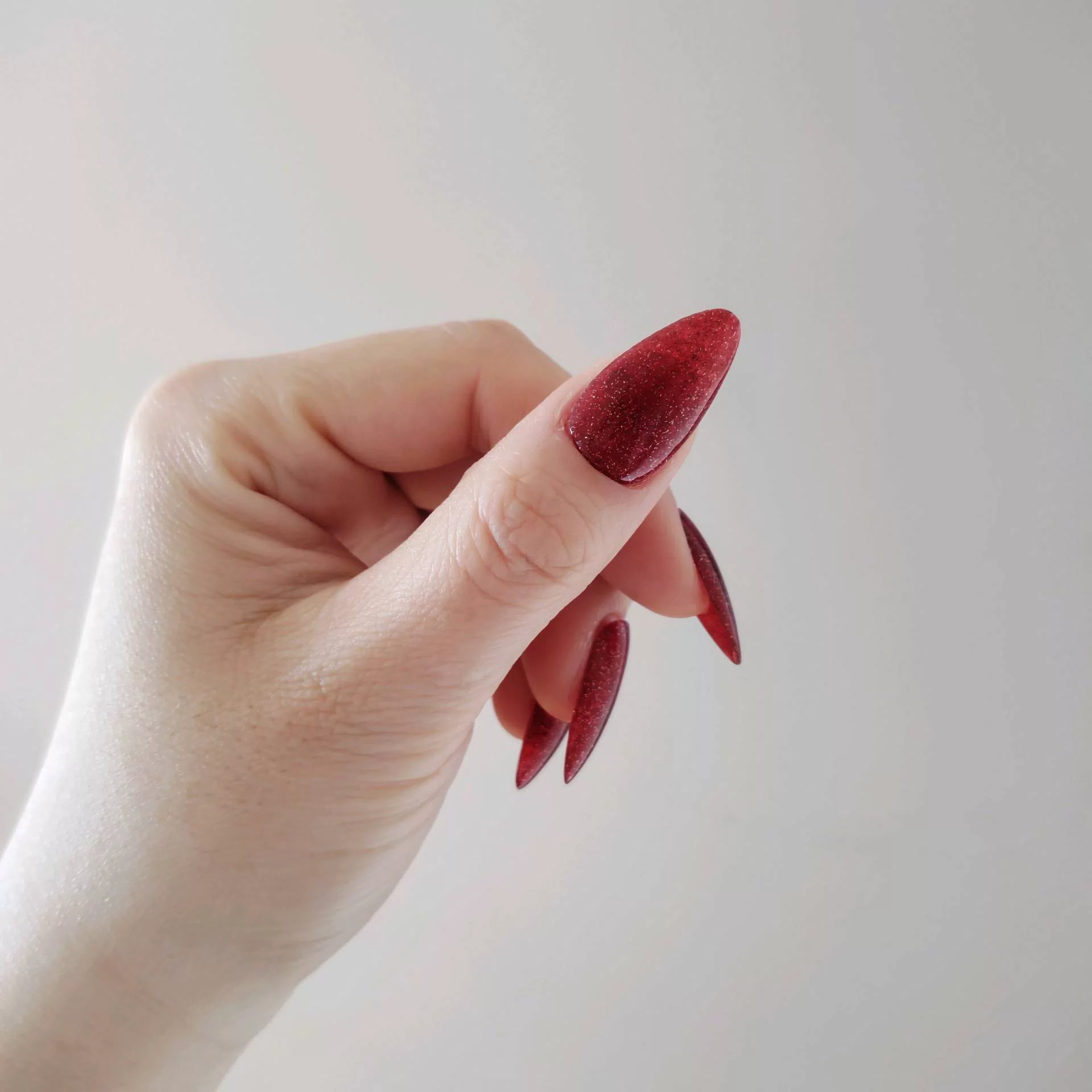 A close-up of a hand showcasing long, tapered stiletto-almond press-on nails coated in a deep, luxurious ruby red magnetic cat-eye shimmer that reflects light with a rich, multi-dimensional velvet finish. — photo 2