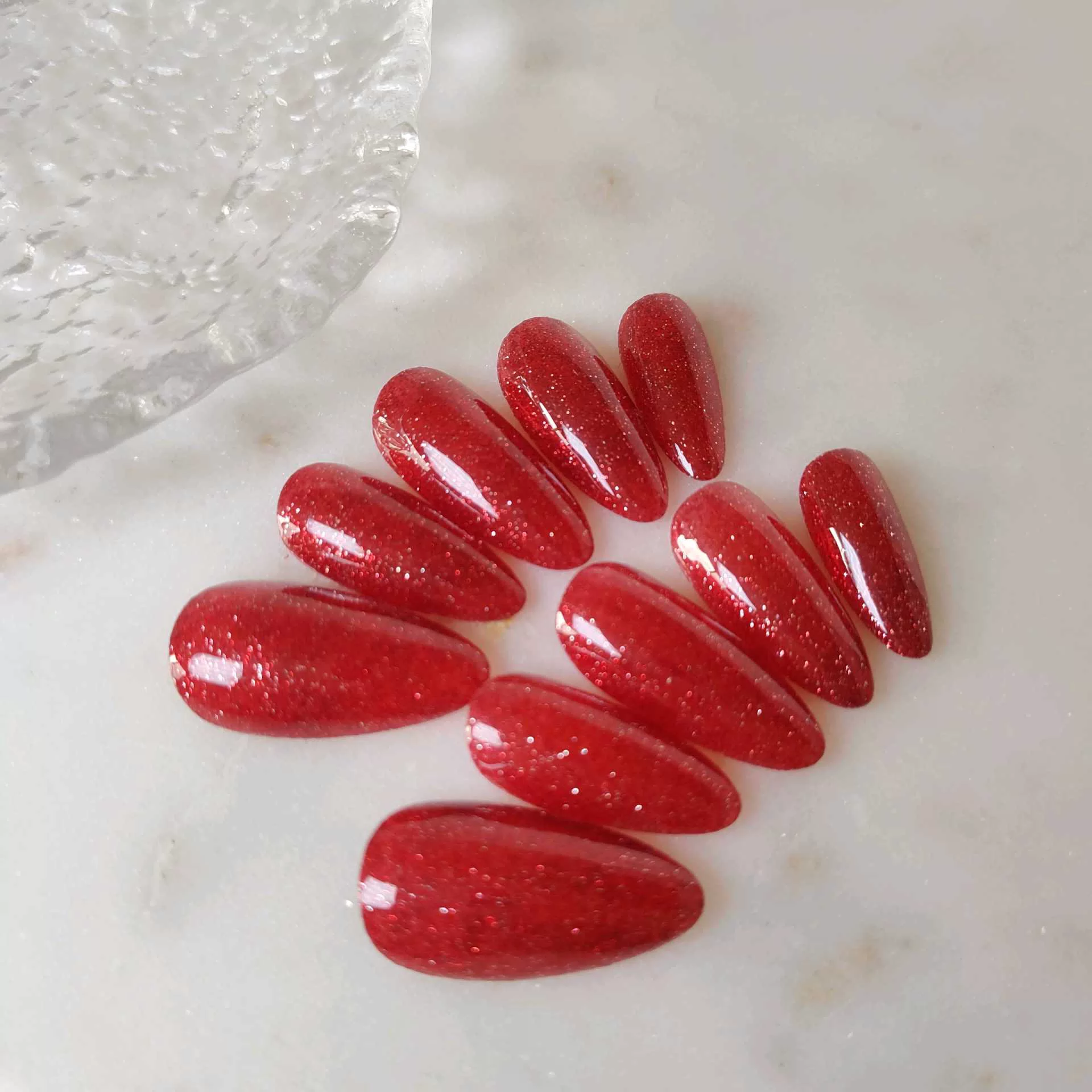 A close-up of a hand showcasing long, tapered stiletto-almond press-on nails coated in a deep, luxurious ruby red magnetic cat-eye shimmer that reflects light with a rich, multi-dimensional velvet finish. — photo 3
