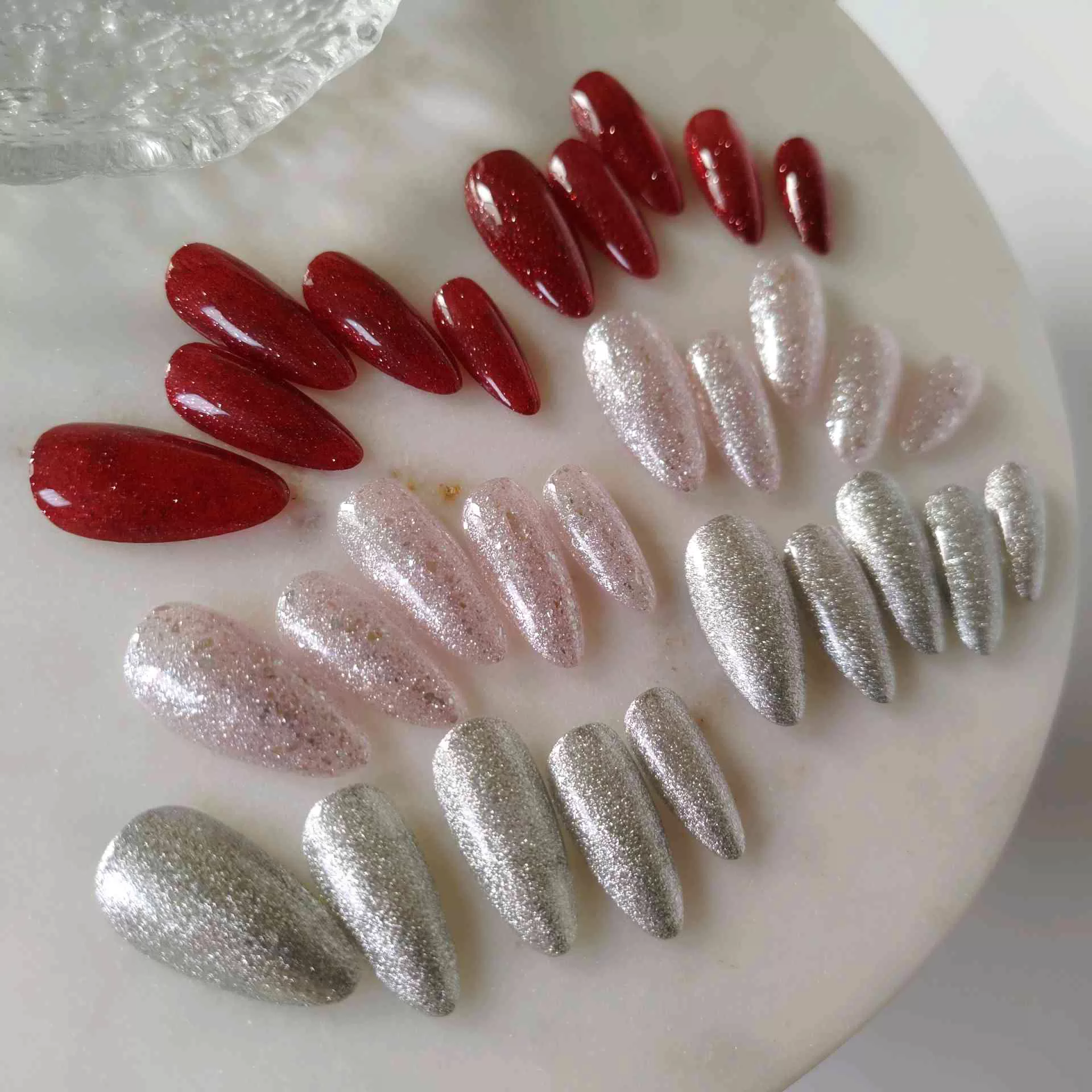 A close-up of a hand showcasing long, tapered stiletto-almond press-on nails coated in a deep, luxurious ruby red magnetic cat-eye shimmer that reflects light with a rich, multi-dimensional velvet finish. — photo 4
