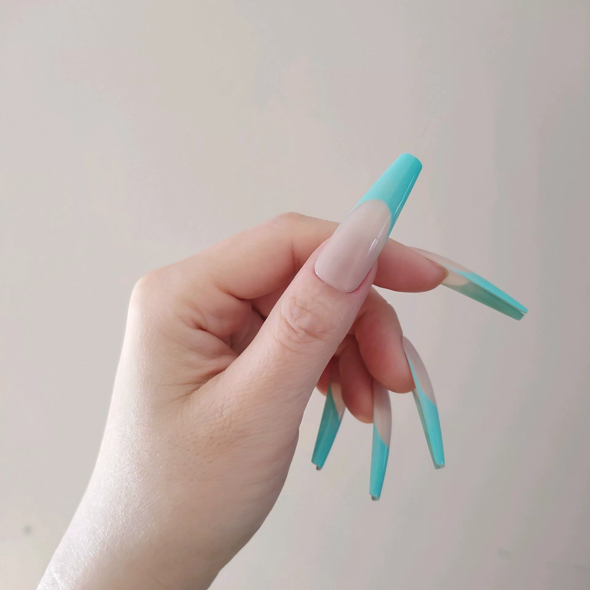 A close-up of a hand showcasing extra-long, square press-on nails featuring a matte nude base and vibrant turquoise-teal French tips aligned in a clean, high-contrast smile line. — photo 2