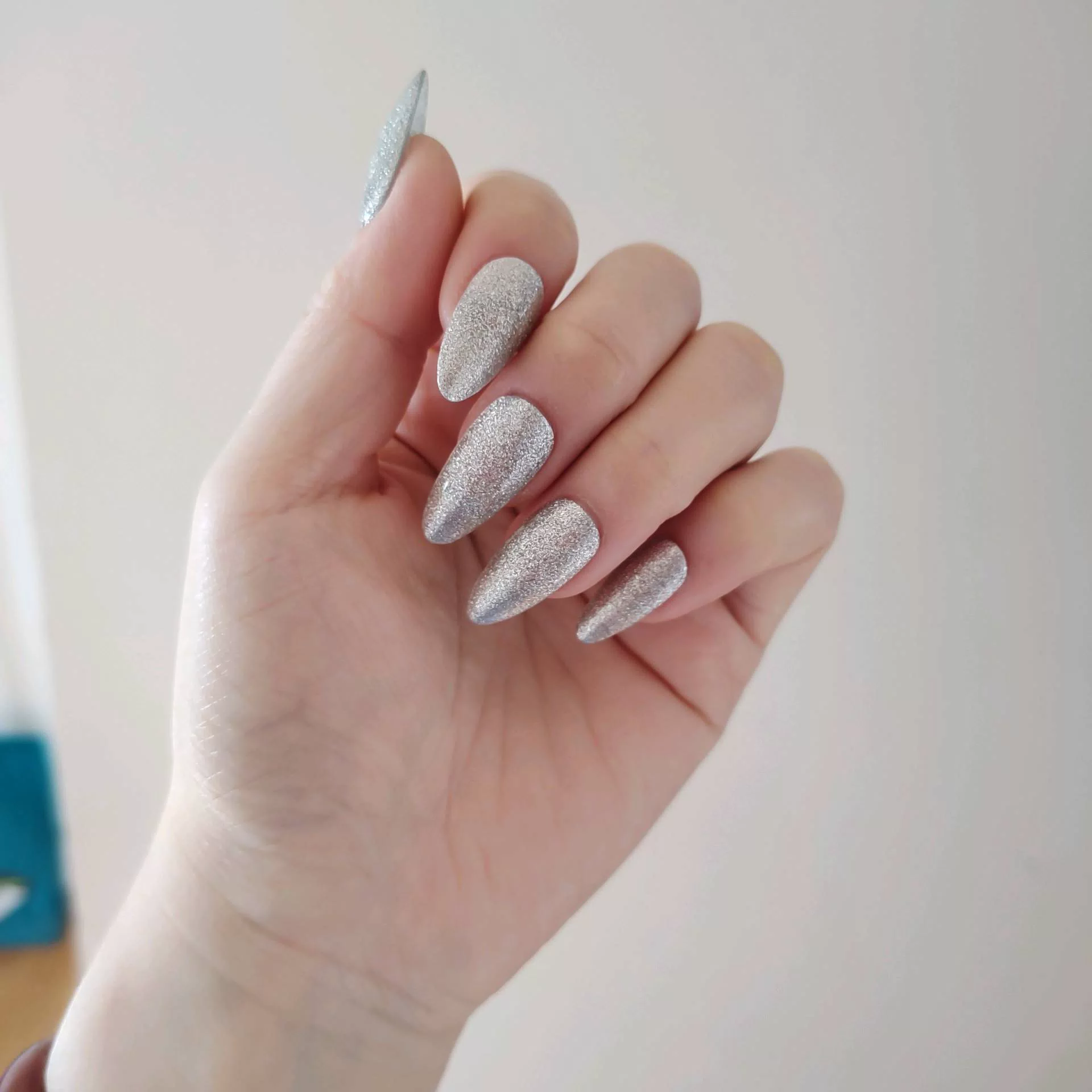 A close-up of a hand showcasing long, tapered stiletto-almond press-on nails featuring a luxurious, dimensional silver-charcoal velvet cat-eye magnetic shimmer that shifts dynamically in the light.